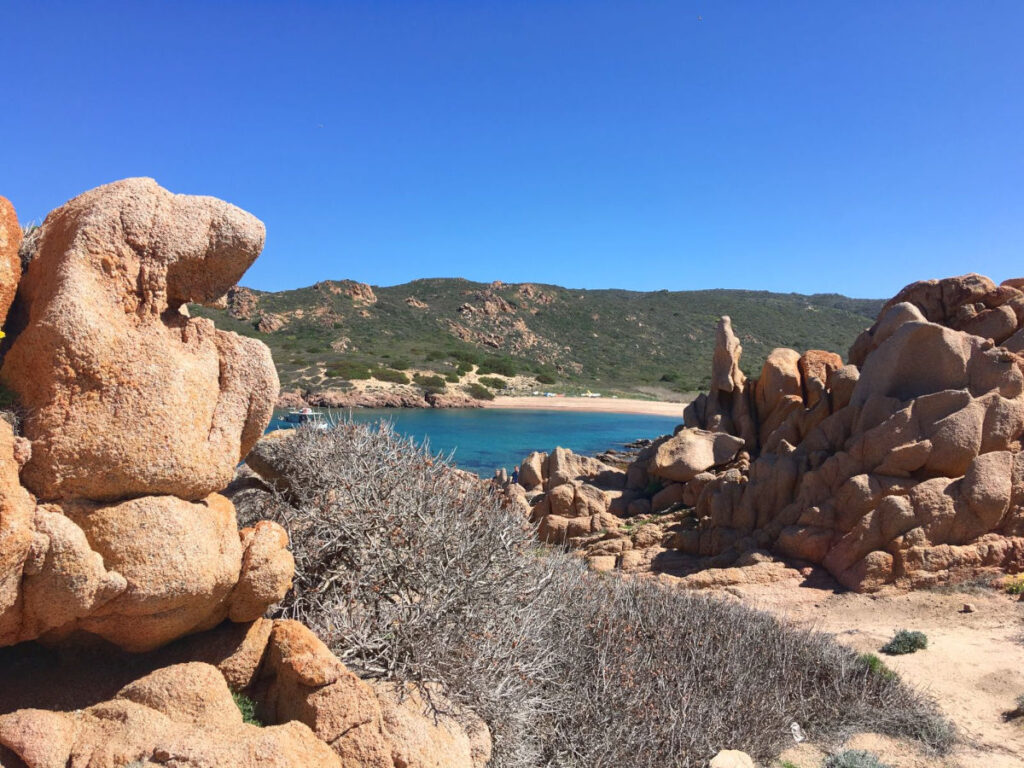 Rote Granitfelsen mit Blick auf eine türkisfarbene Bucht am Hausstrand.